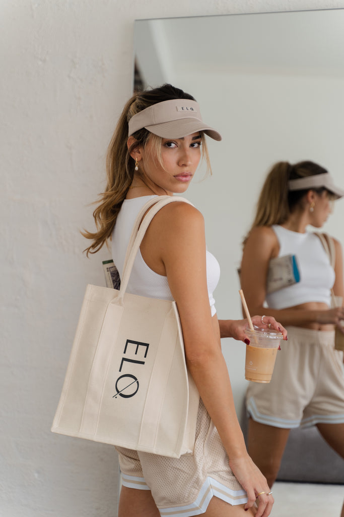 Female model wearing oat beige visor hat with canvas tote bag