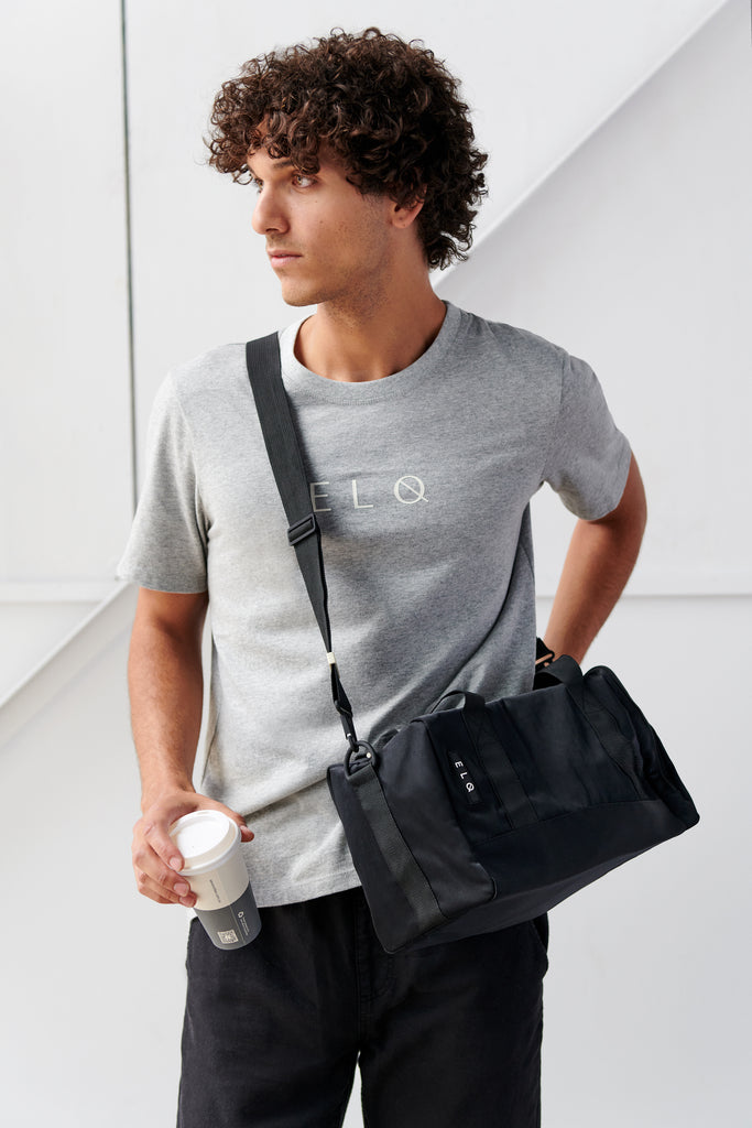 Male model wearing grey tshirt and black crossbody bag