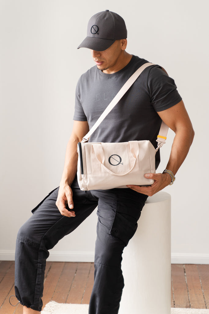 Model wearing black tee, baseball black cap and nude duffle bag