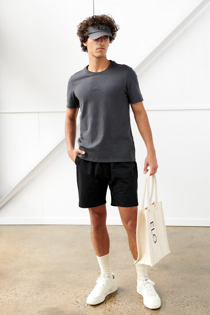 Male model holding Utility Canvas Tote Bag in Vanilla with black visor and black tee